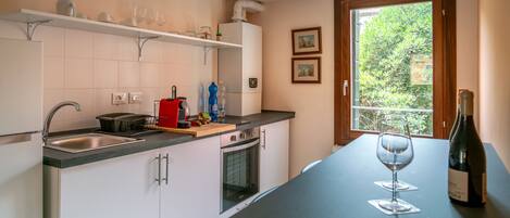 A kitchen with a sink, stove, oven, and a window with a view of greenery.