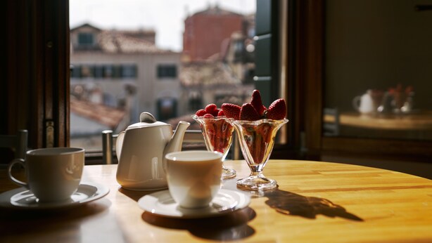 A table with a cup, a teapot, and a glass with strawberries. - Palazzo San Luca (Venice)