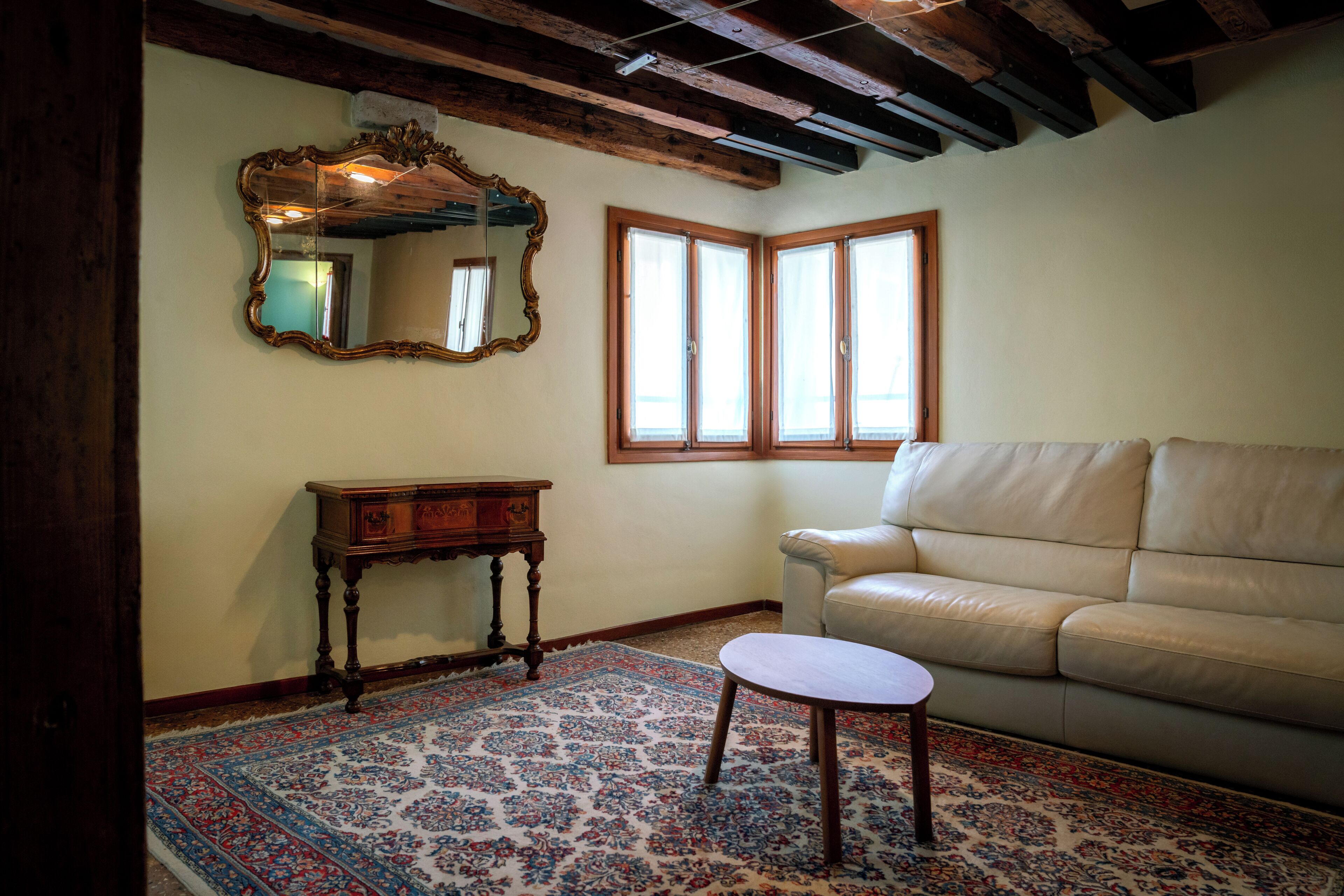 A room with a wooden ceiling, a large mirror, a beige sofa, a small table, and a patterned rug.
