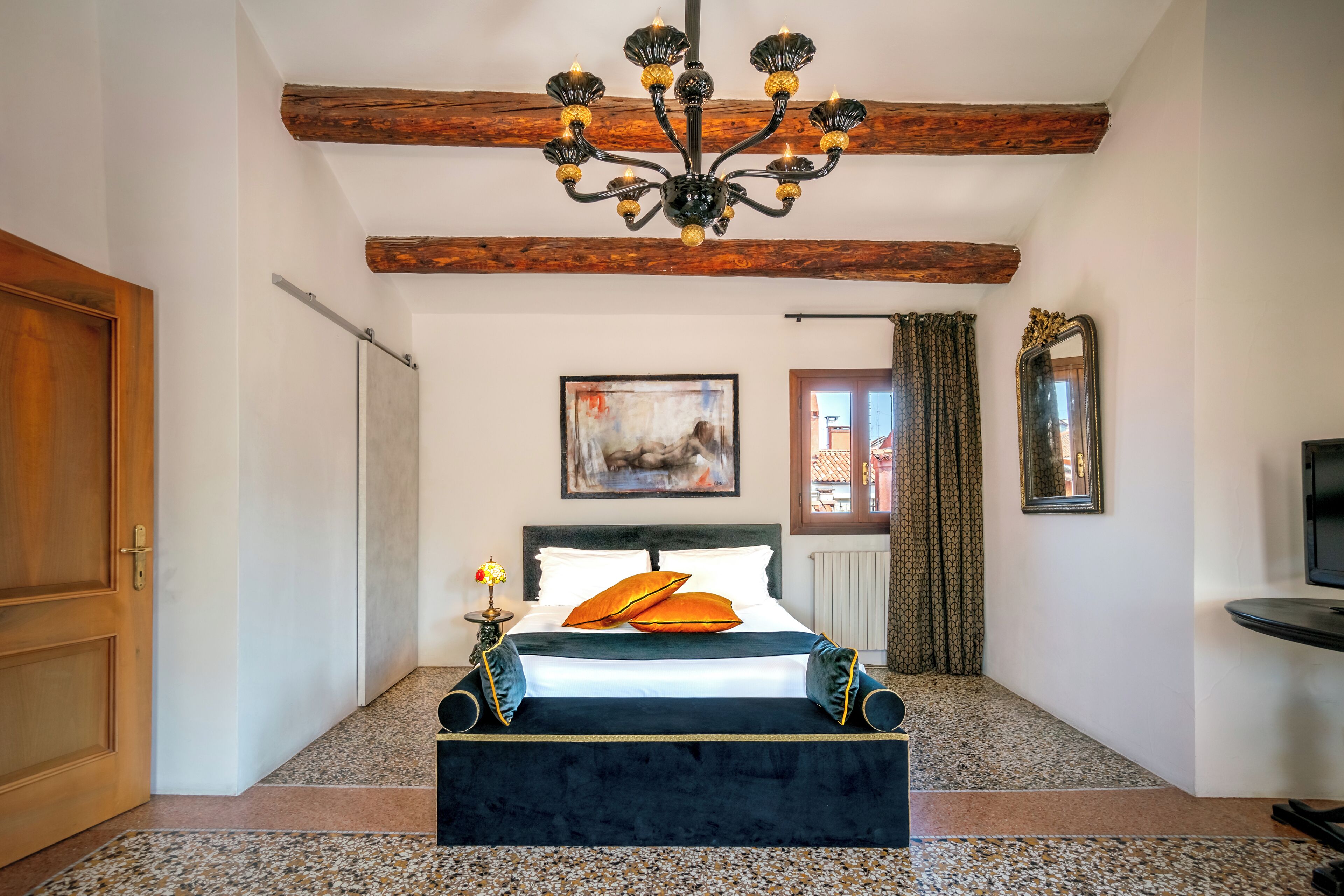 Ein Schlafzimmer mit einem großen Bett, einer Kristallleuchtre, einem Gemälde an der Wand und einem Holzbalken an der Decke.