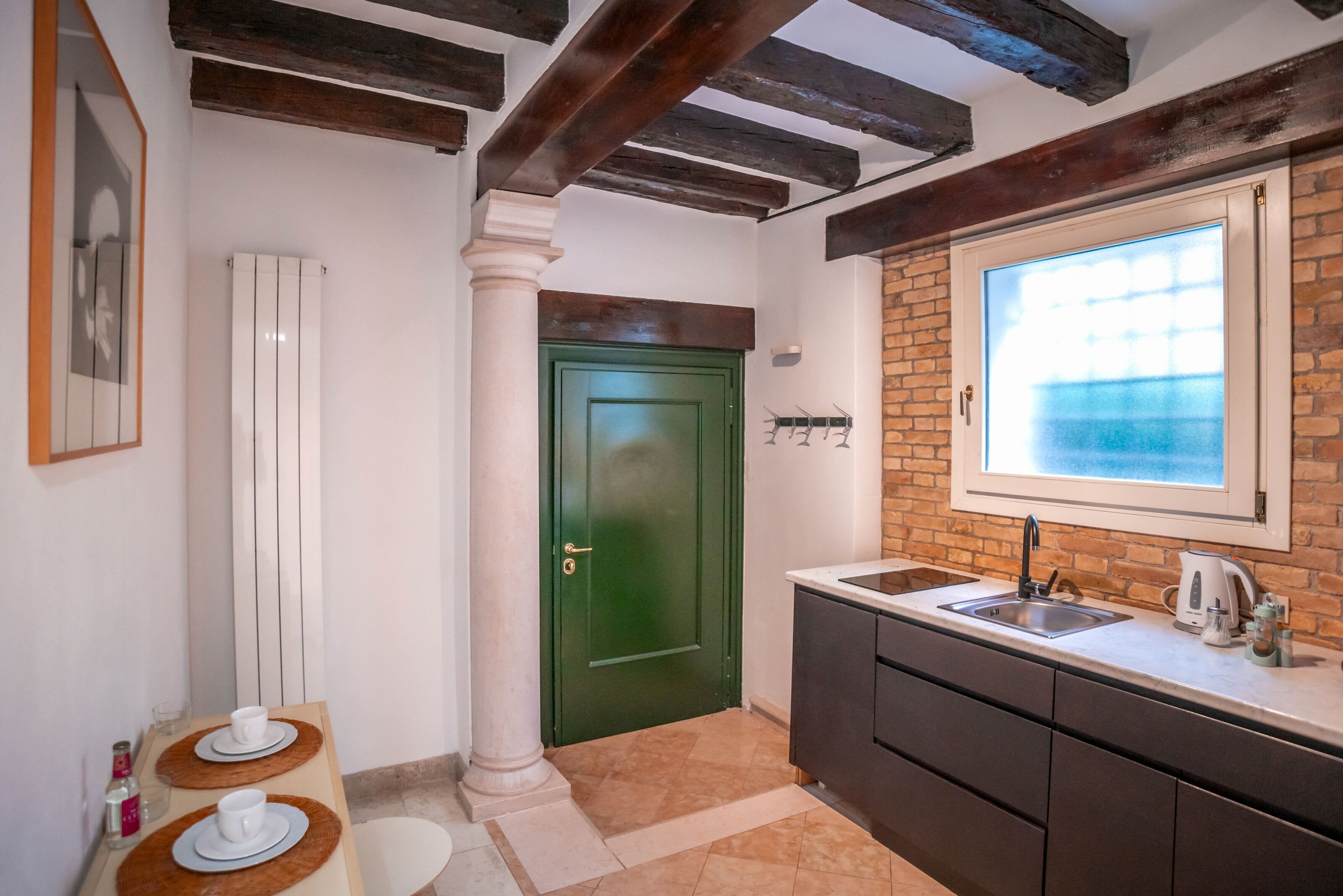 A kitchen with a green door, a window with a view, a sink, and a countertop with a kettle.