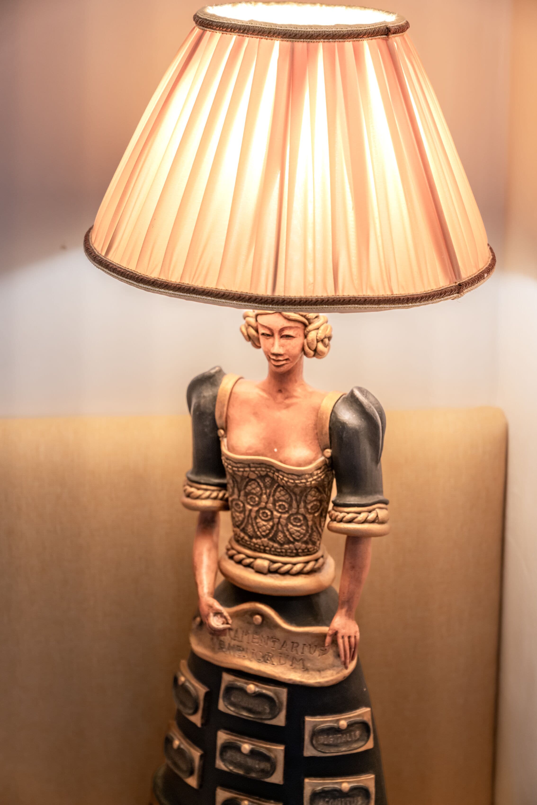 A lamp with a pleated shade and a figure of a woman holding a book.