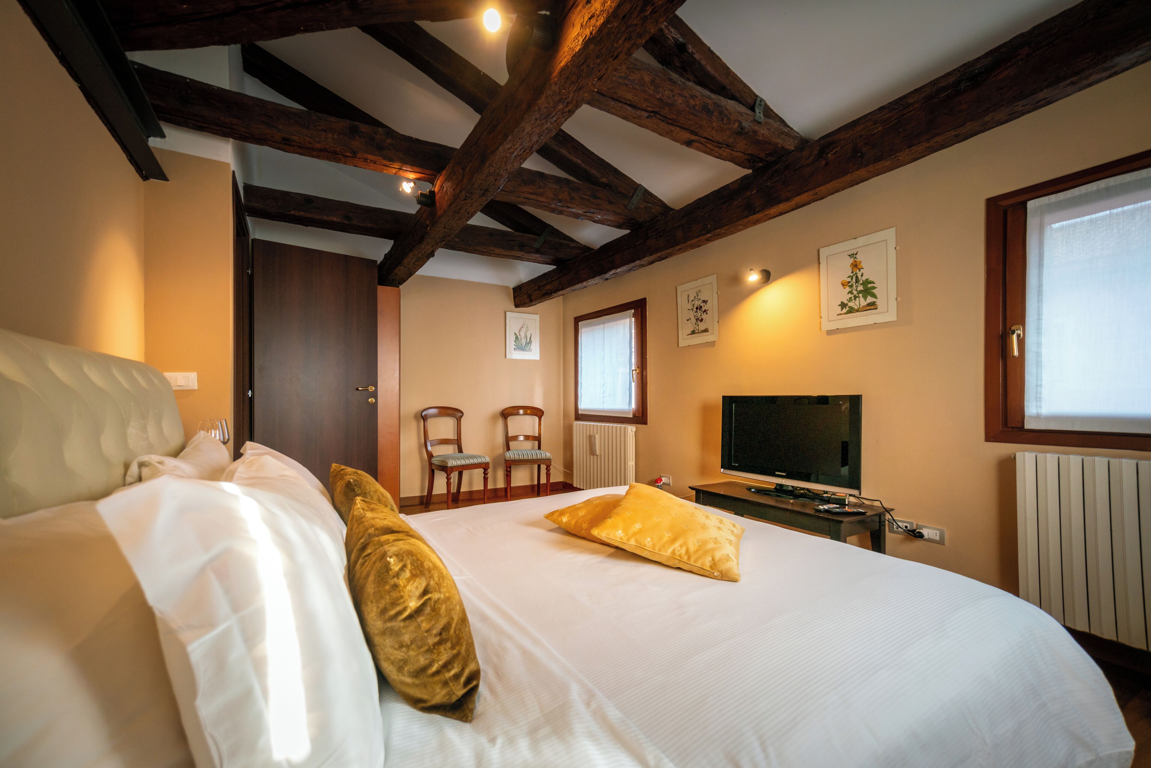 A hotel room with a large bed, wooden beams, a television, and two chairs.