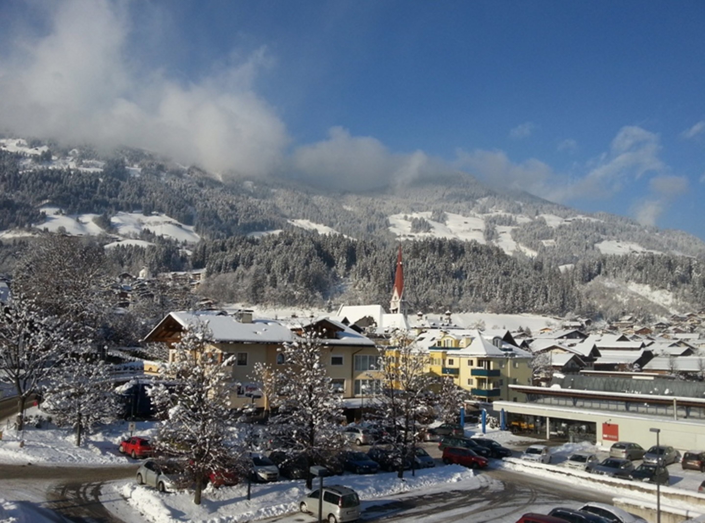 A snow-covered town with buildings and a church, surrounded by mountains.
