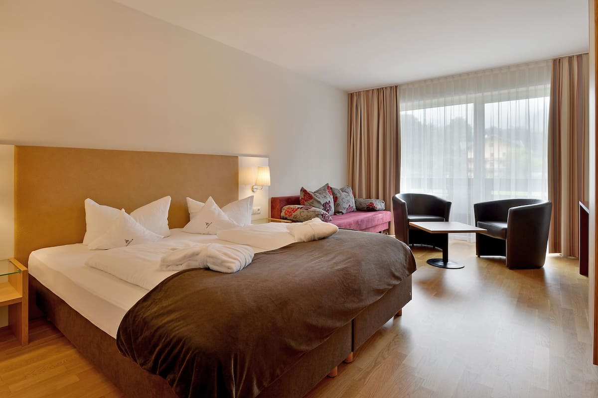 A hotel room with a large bed, a desk, two chairs, and a window with curtains.