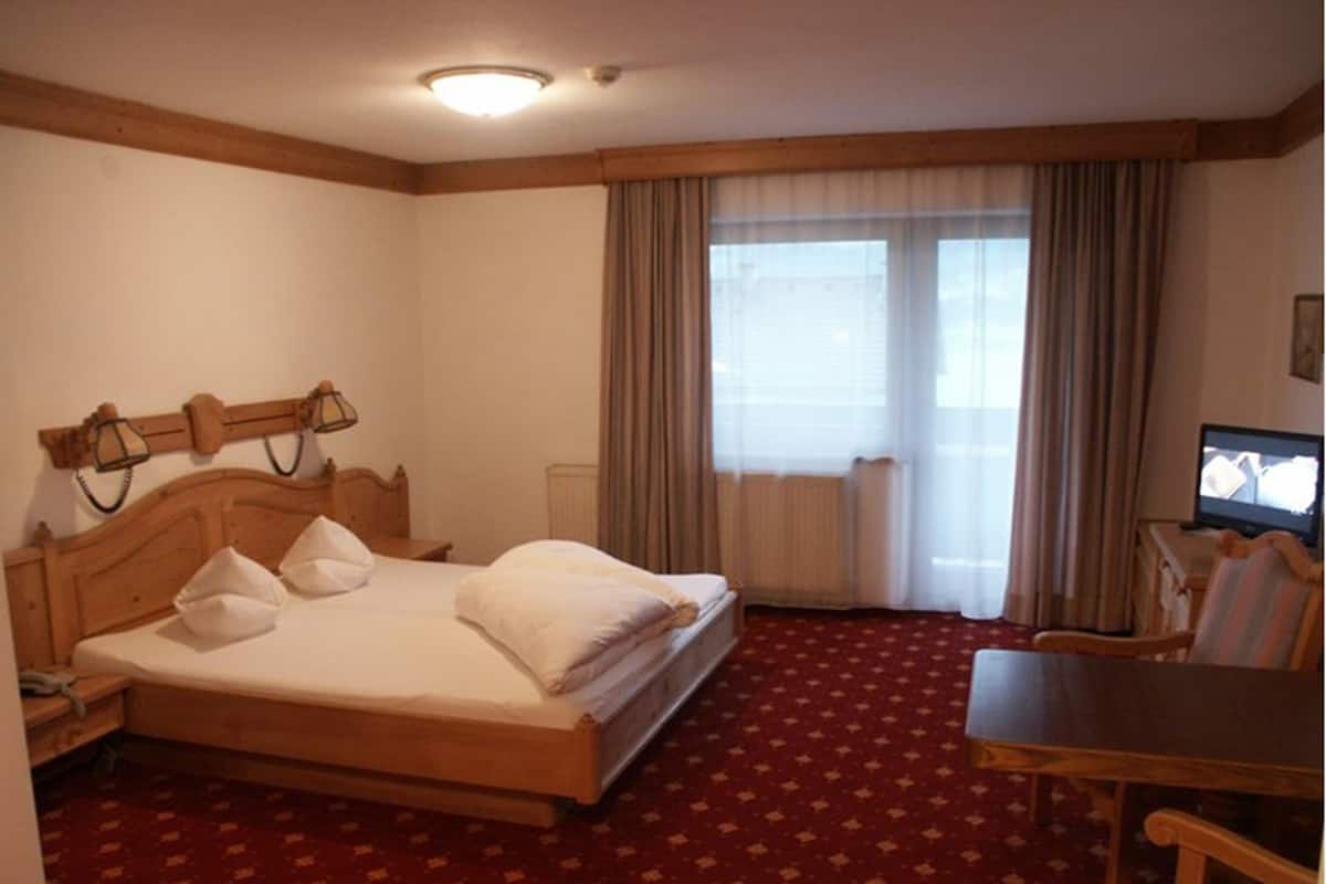 A hotel room with a wooden bed, a desk, a chair, and a television.