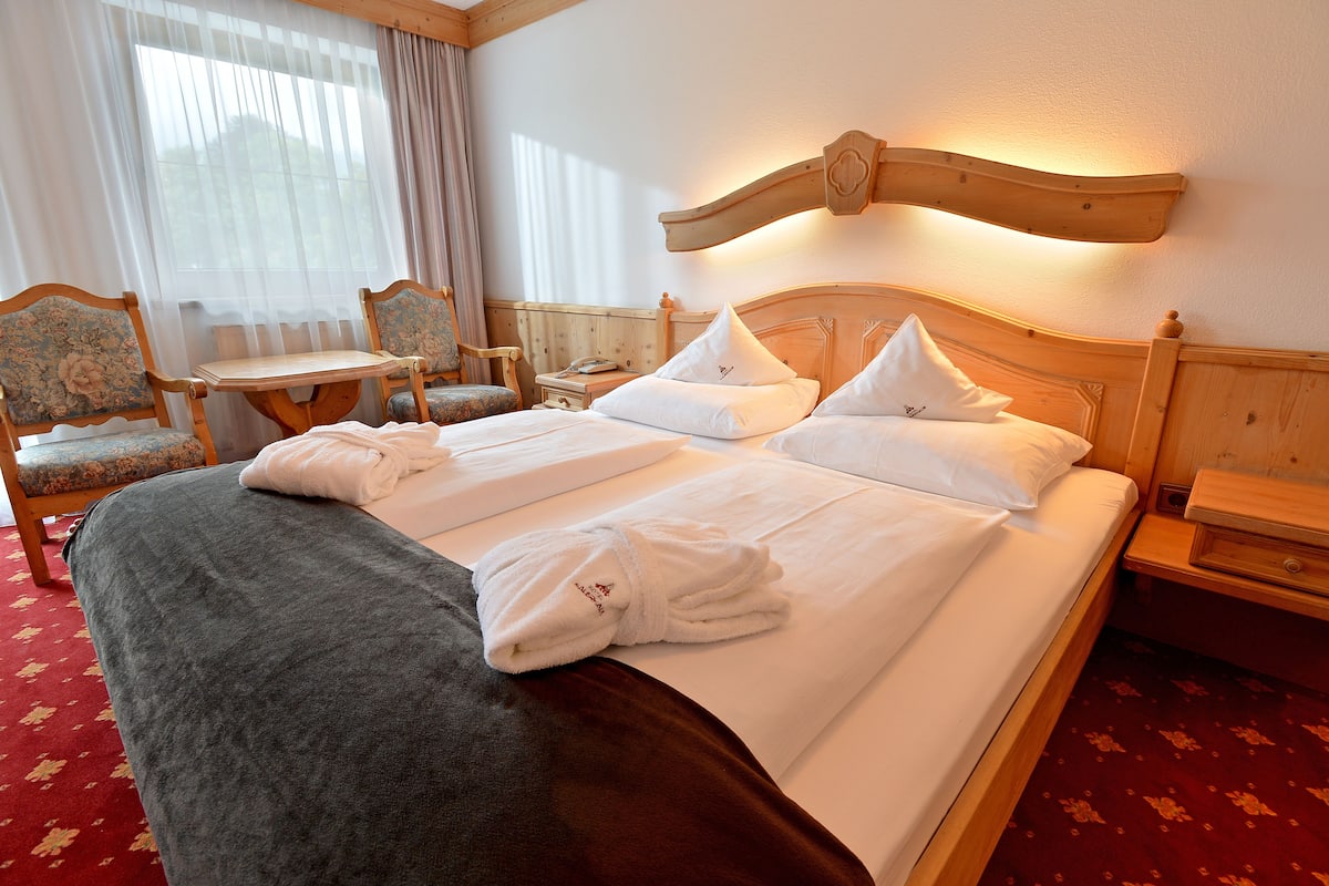 A hotel room with a large bed, two bedside tables, a wooden headboard, and a small table with chairs.