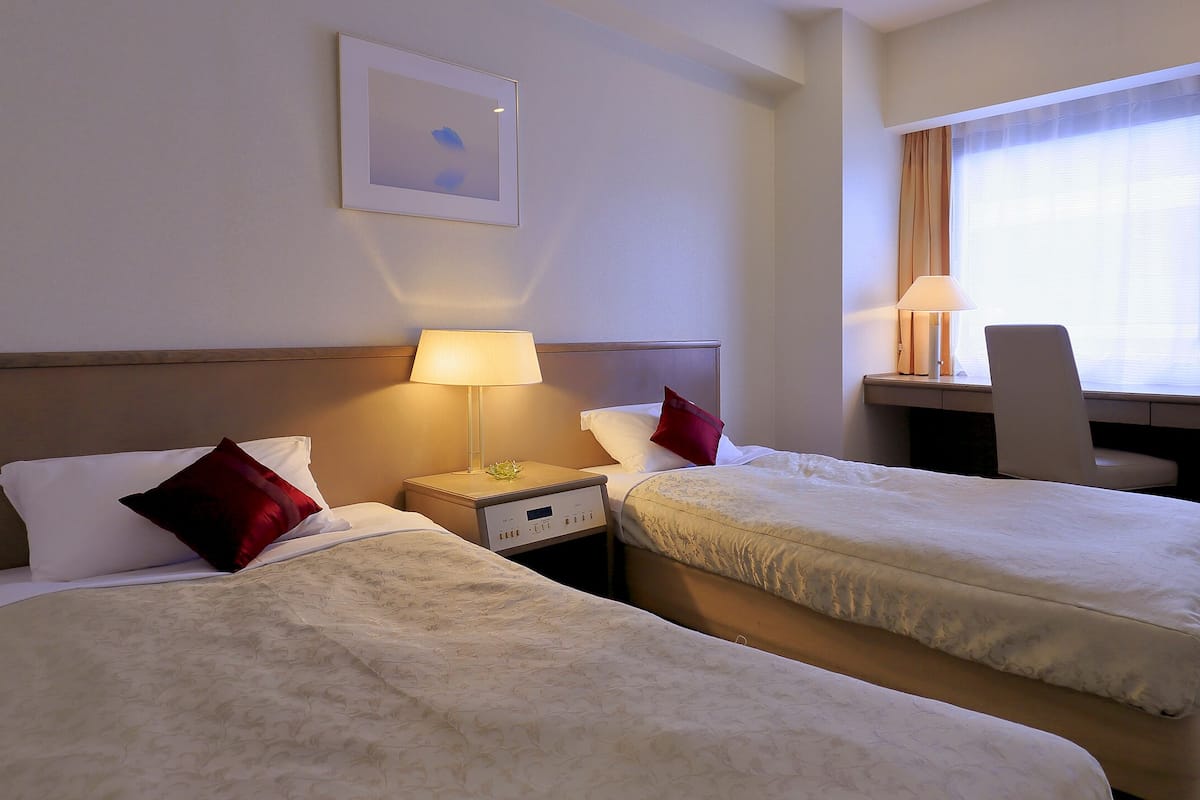 A hotel room with two beds, a desk with a computer, a TV, and a window with curtains.