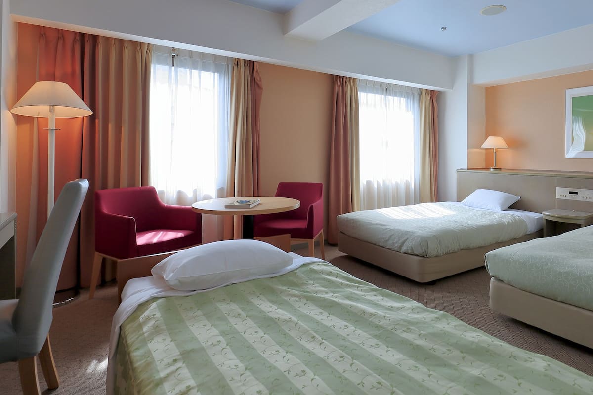 A hotel room with two beds, a desk, a chair, and a window with curtains.