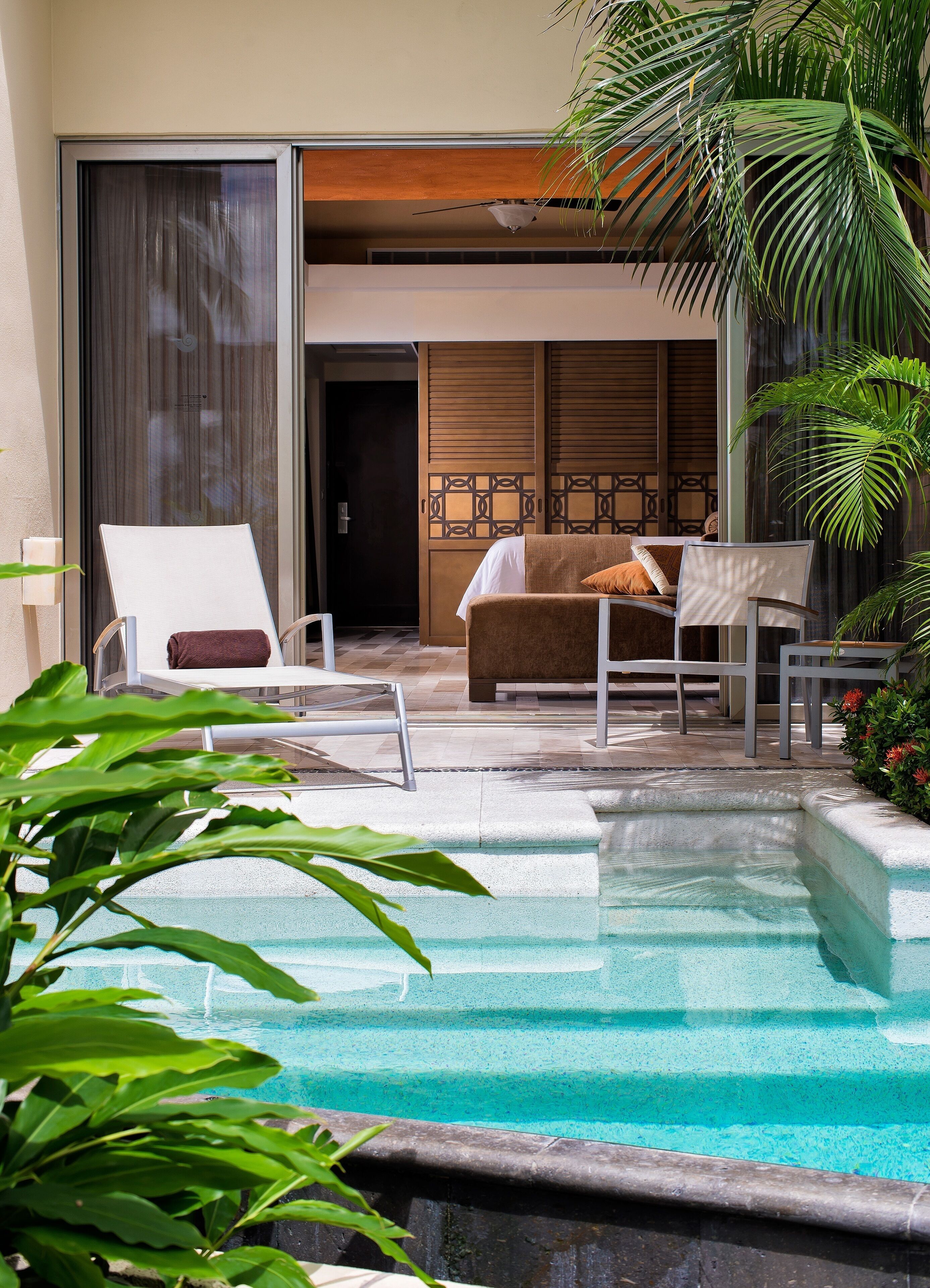 A pool area with a lounge chair, a sofa, and a dining table.