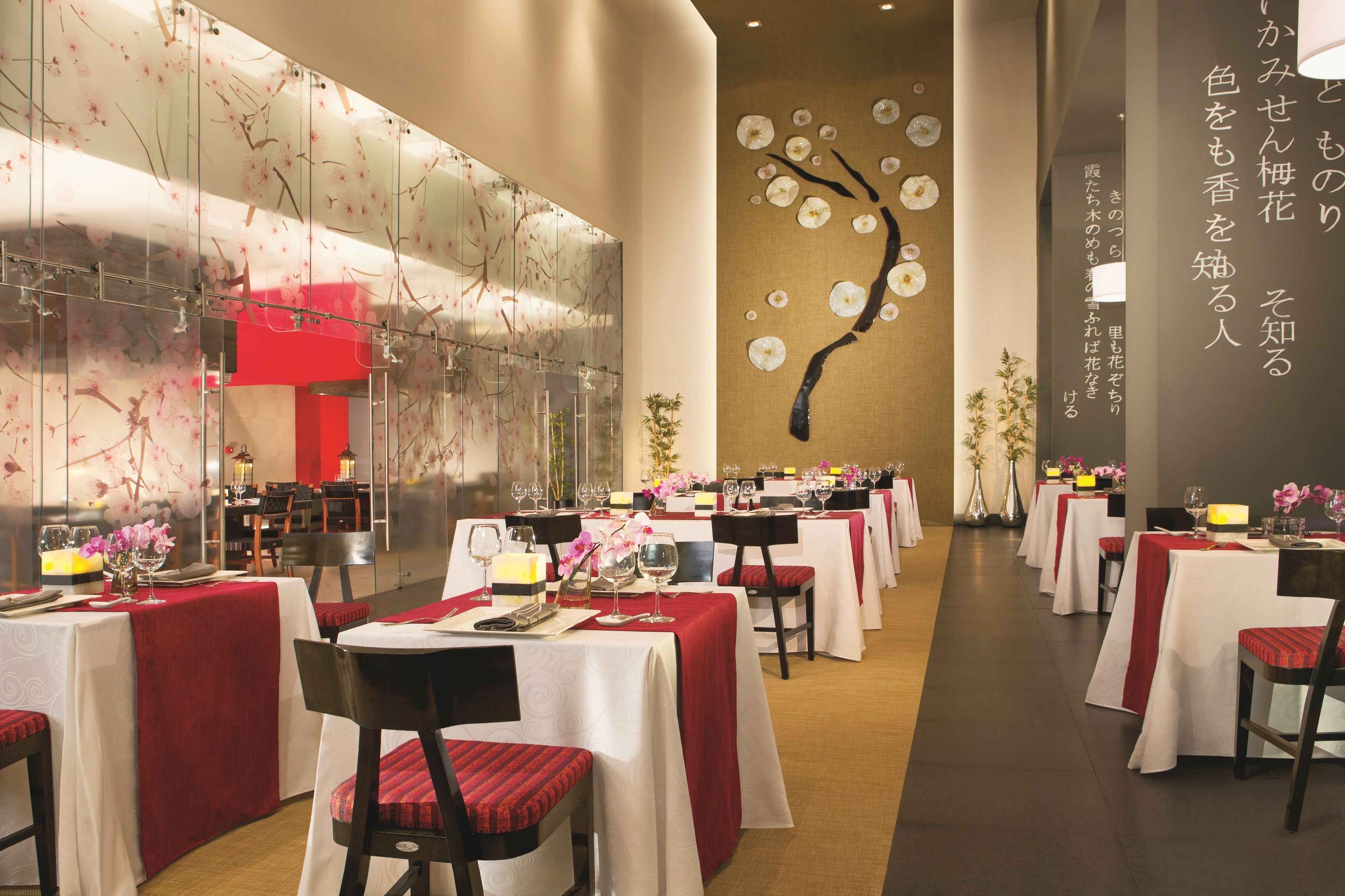 A restaurant with multiple tables, each set with white tablecloths and red chairs.