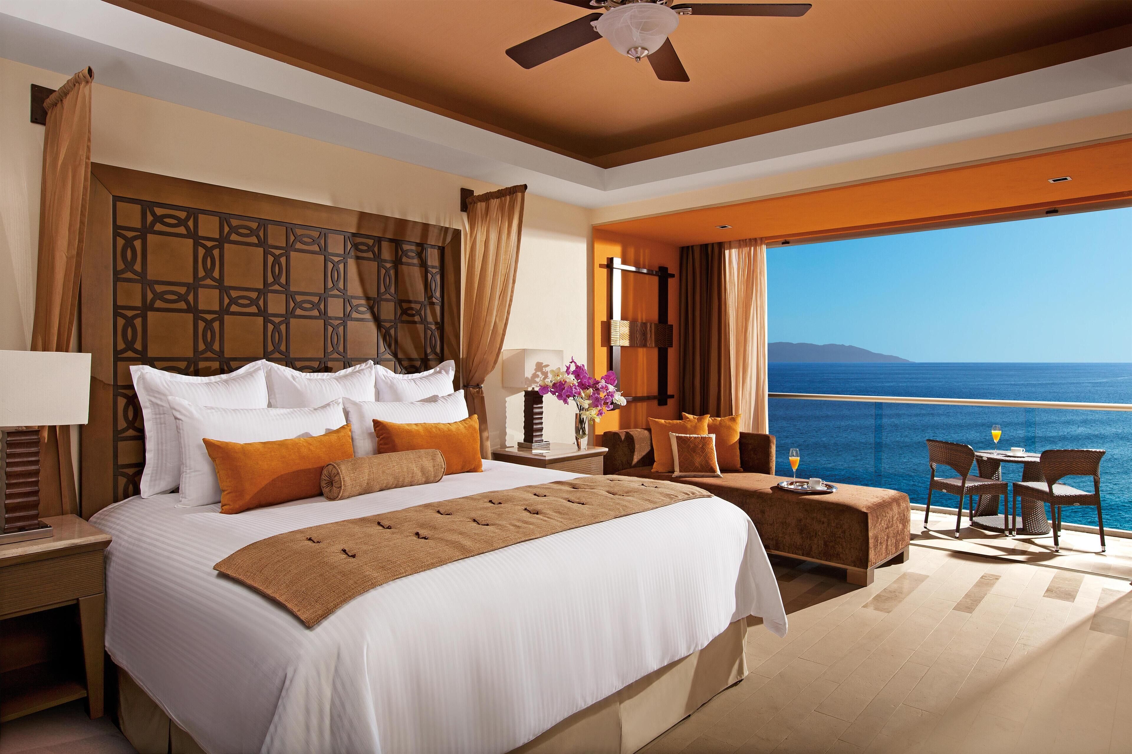 Une chambre d’hôtel dotée d’un grand lit, d’un balcon avec vue sur la mer et d’un coin repas avec des chaises et une table.