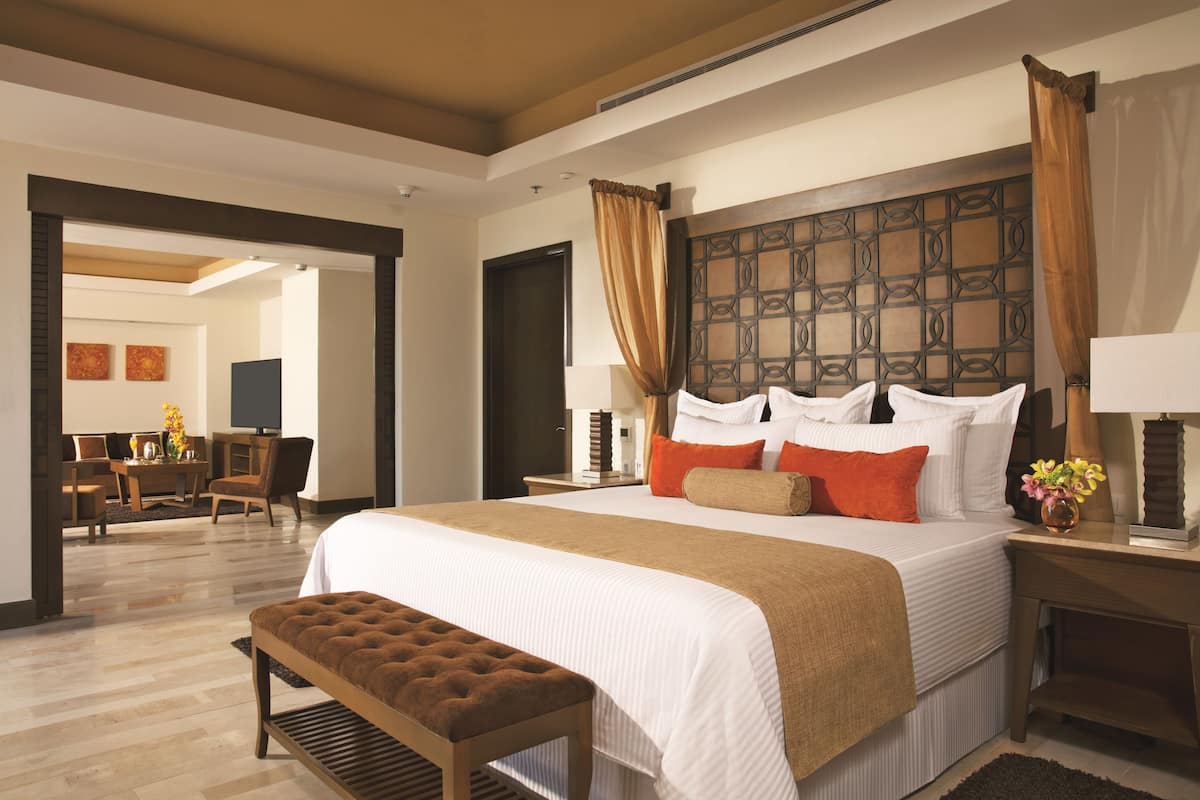 A hotel room with a large bed, a wooden bench, a desk, and a television.