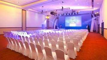 Une salle de conférence avec des rangées de chaises blanches, une scène sur laquelle est installé un écran affichant le mot « Secrets », et un tapis rouge.