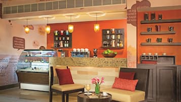 Un acogedor interior de cafetería con mesas, una máquina de café y una vitrina.