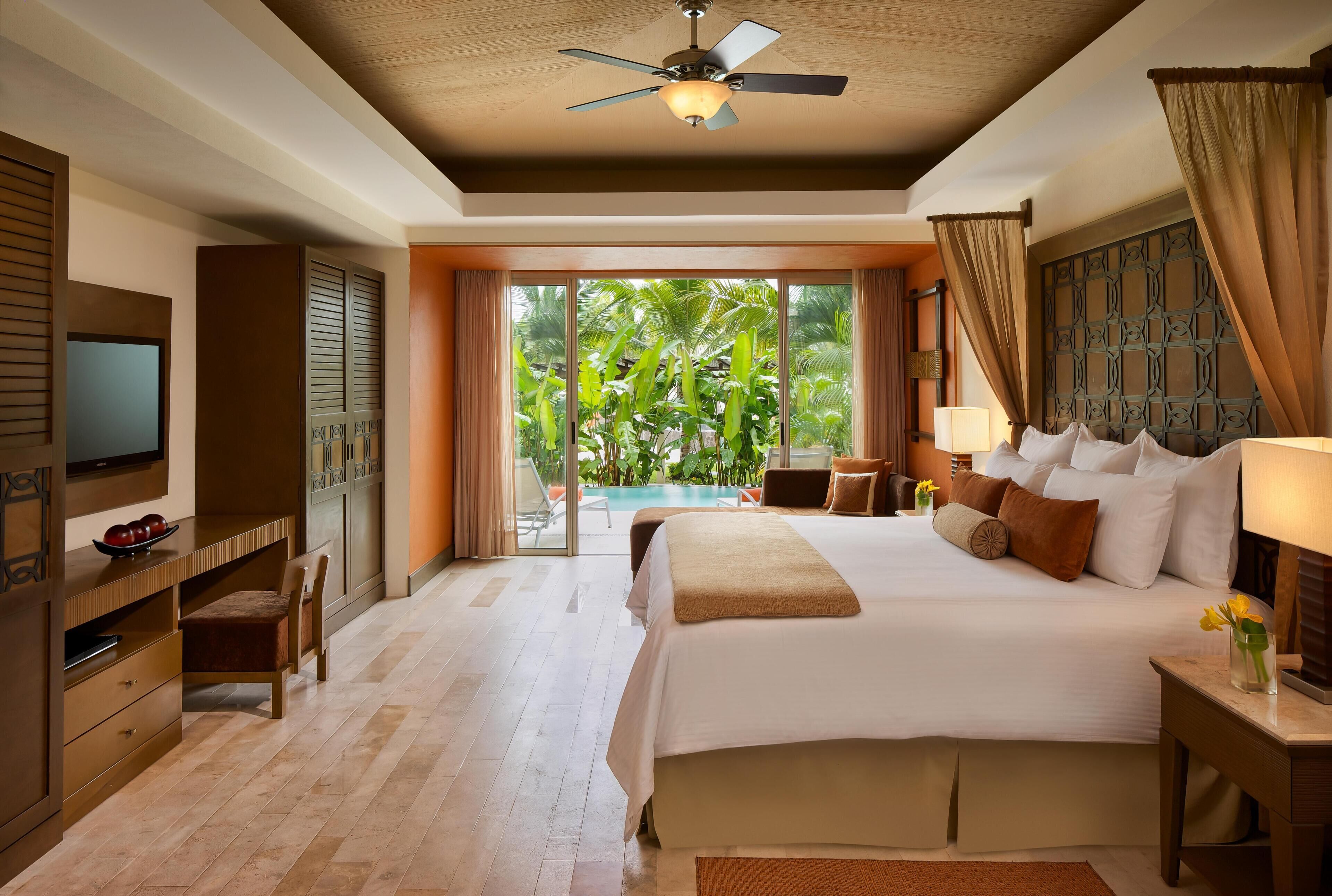 A hotel room with a large bed, a TV, a desk, and a view of a swimming pool.