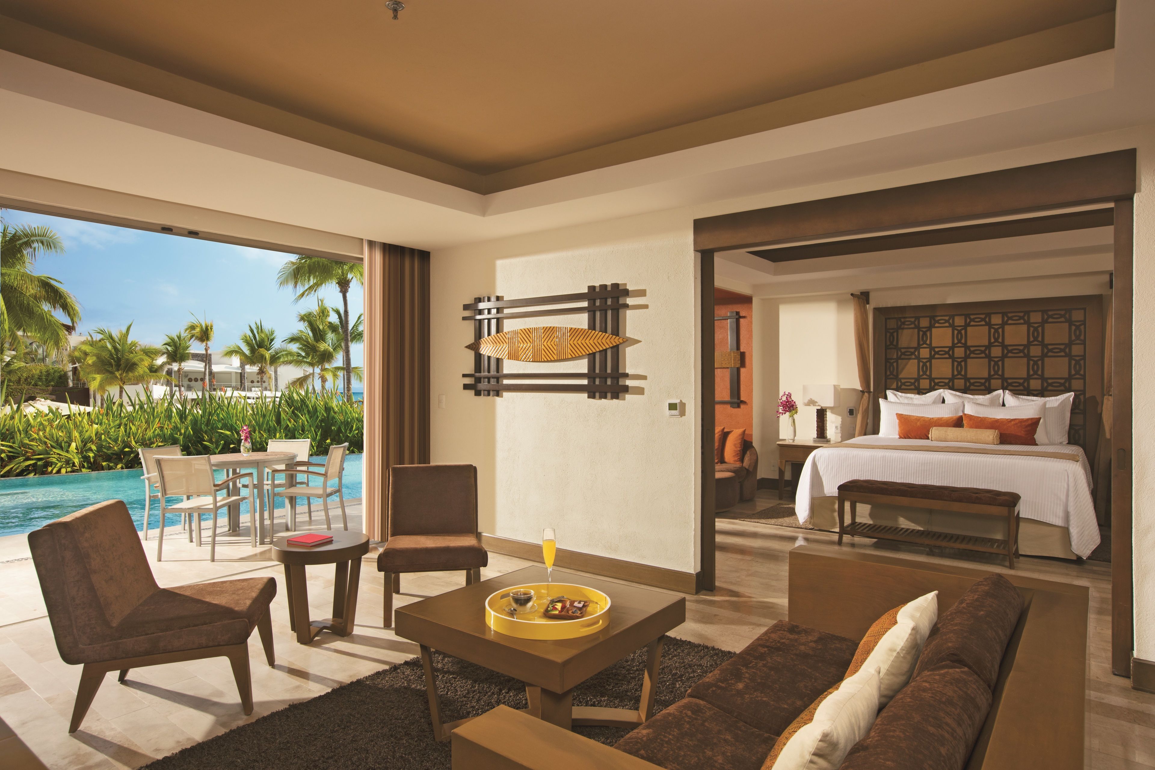 A modern hotel room with a pool view, a dining area, and a bedroom with a large bed and a headboard.