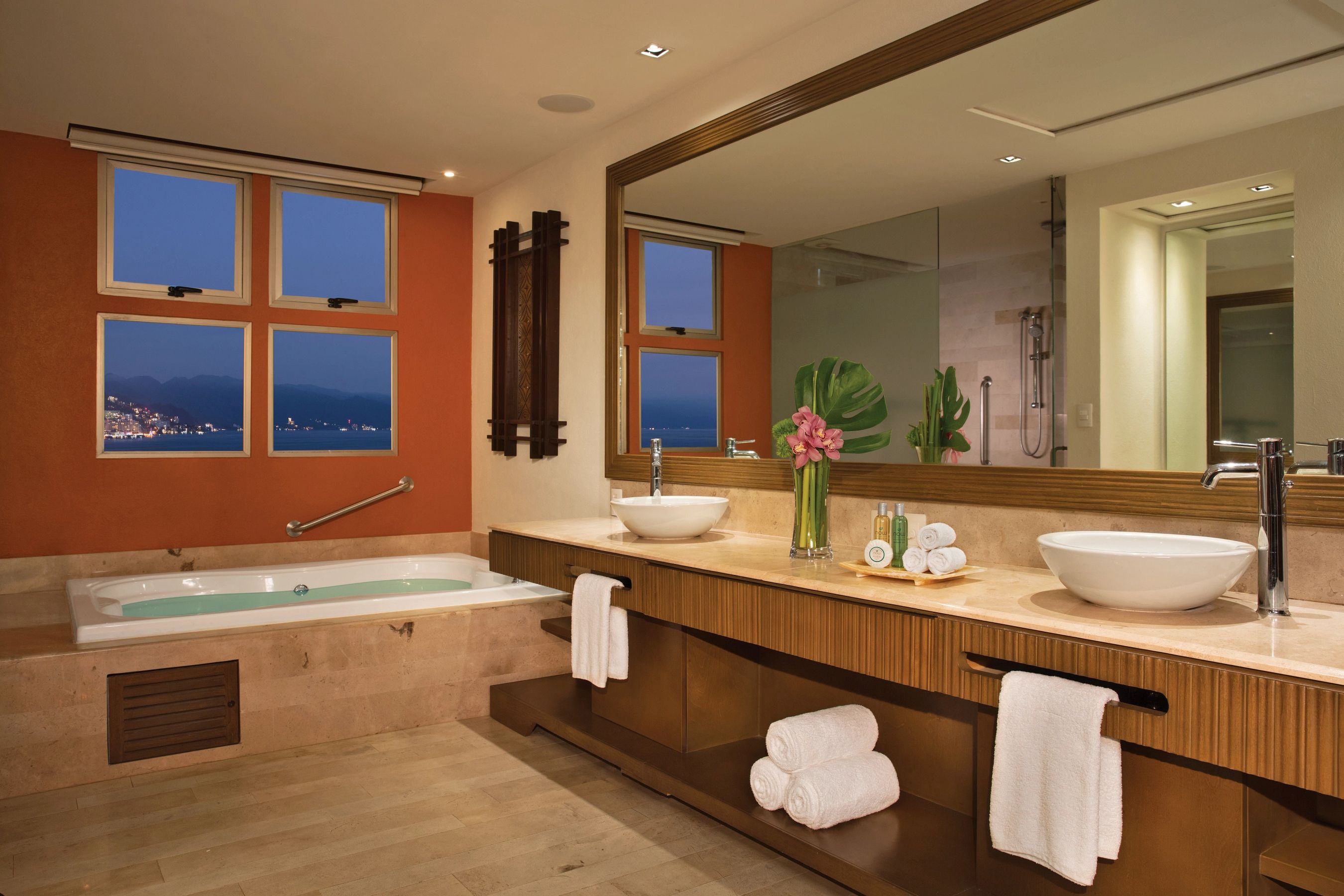 Ein modernes Badezimmer mit einer großen Badewanne, zwei Waschbecken, einem großen Spiegel und einem Fenster mit Blick auf die Stadt.