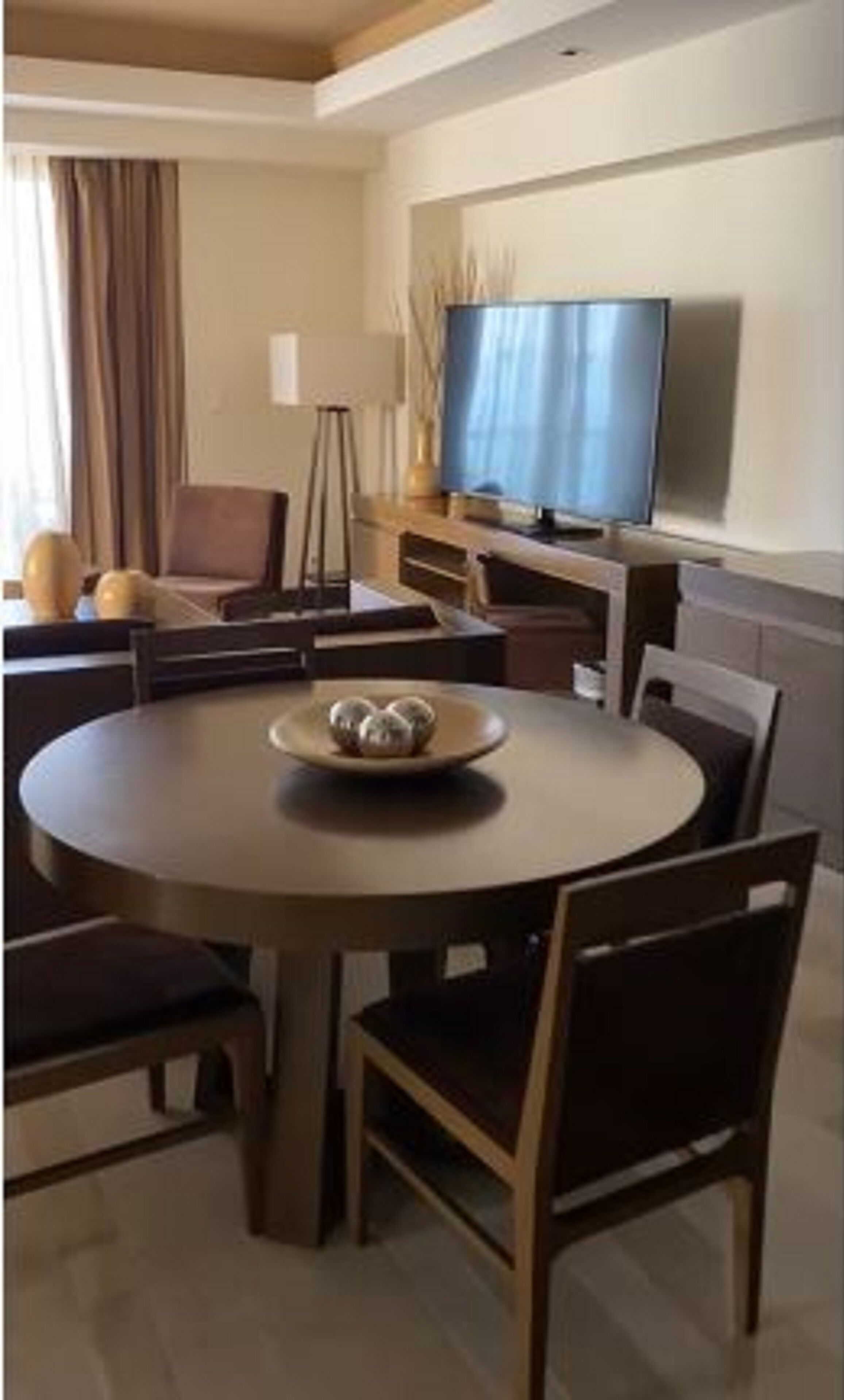 A modern dining area with a round table, chairs, and a bowl of fruit.