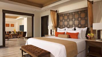 A hotel room with a large bed, a wooden headboard, a bench, a desk, and a TV.