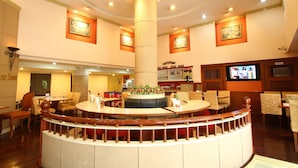 Un vestíbulo de hotel con una mesa redonda central, varias zonas de estar y una pantalla de televisión.