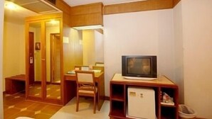 Una habitación de hotel compacta con un escritorio pequeño, una silla, televisor y un refrigerador minibar.