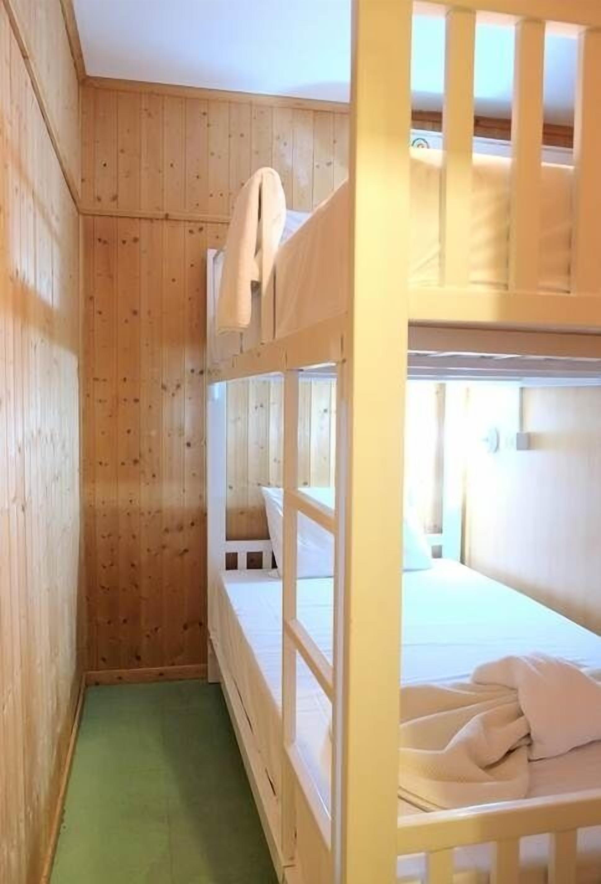 Quarto com beliche, paredes de madeira e chão verde.