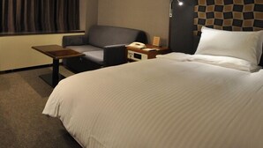 A hotel room with a large bed, a desk, a chair, and a nightstand with a phone. - Mito Keisei Hotel (Mito)