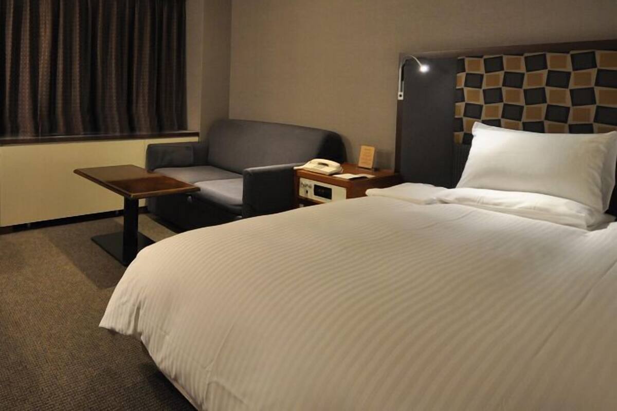 A hotel room with a large bed, a desk, a chair, and a nightstand with a phone.