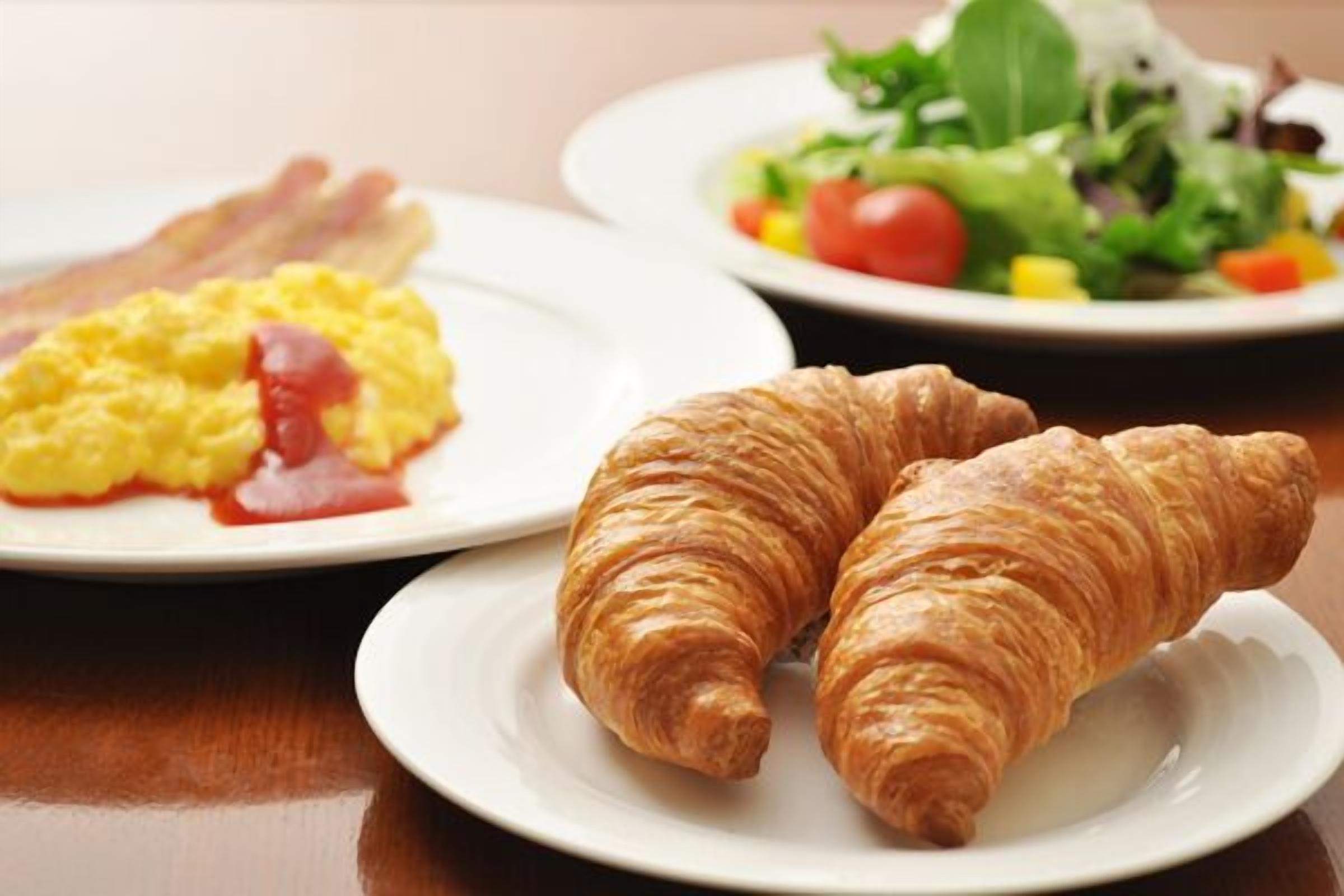 Une table dressée pour le petit-déjeuner avec des croissants, des œufs brouillés, du bacon et une salade.