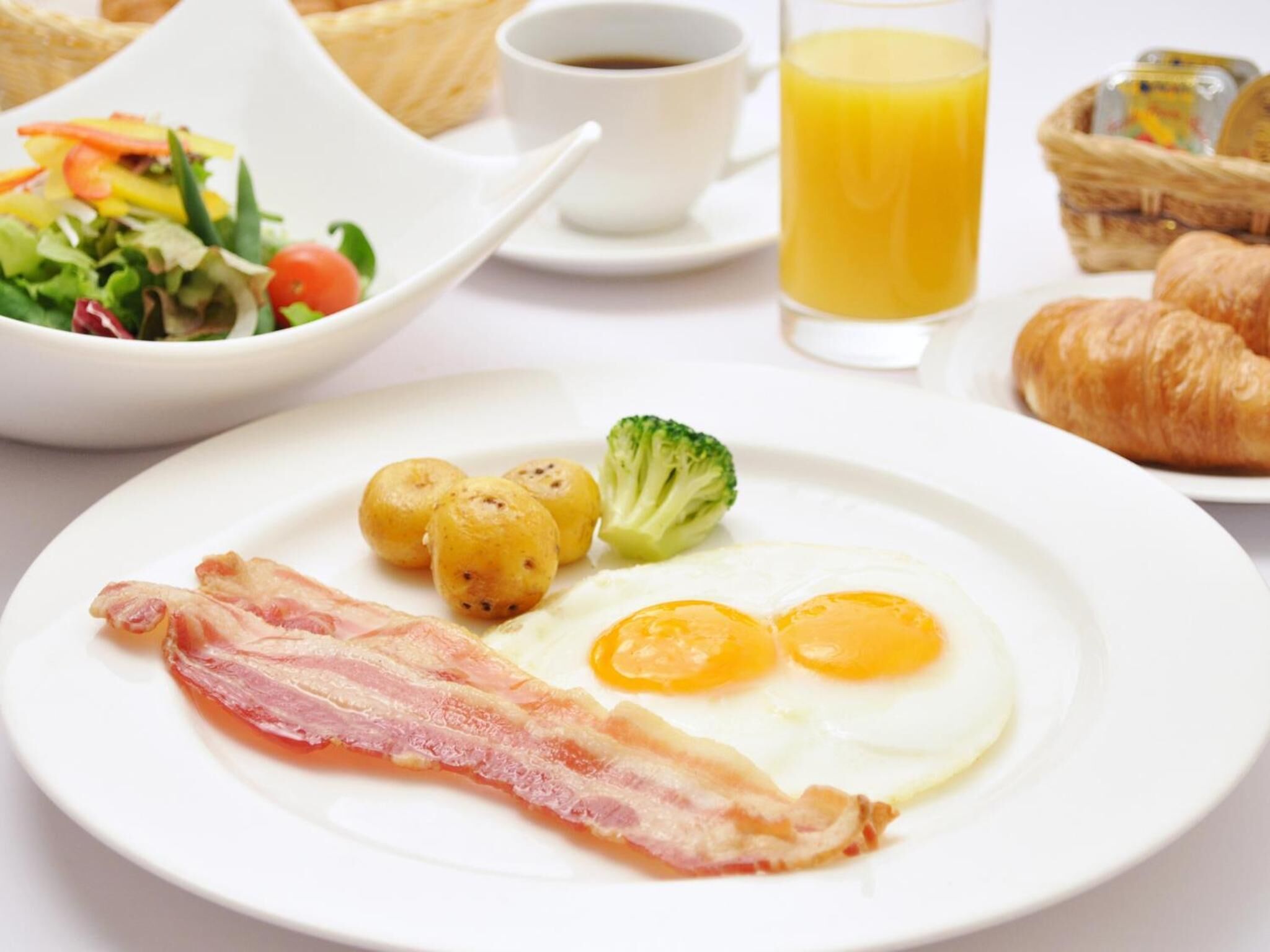 A breakfast plate with eggs, bacon, potatoes, and broccoli.