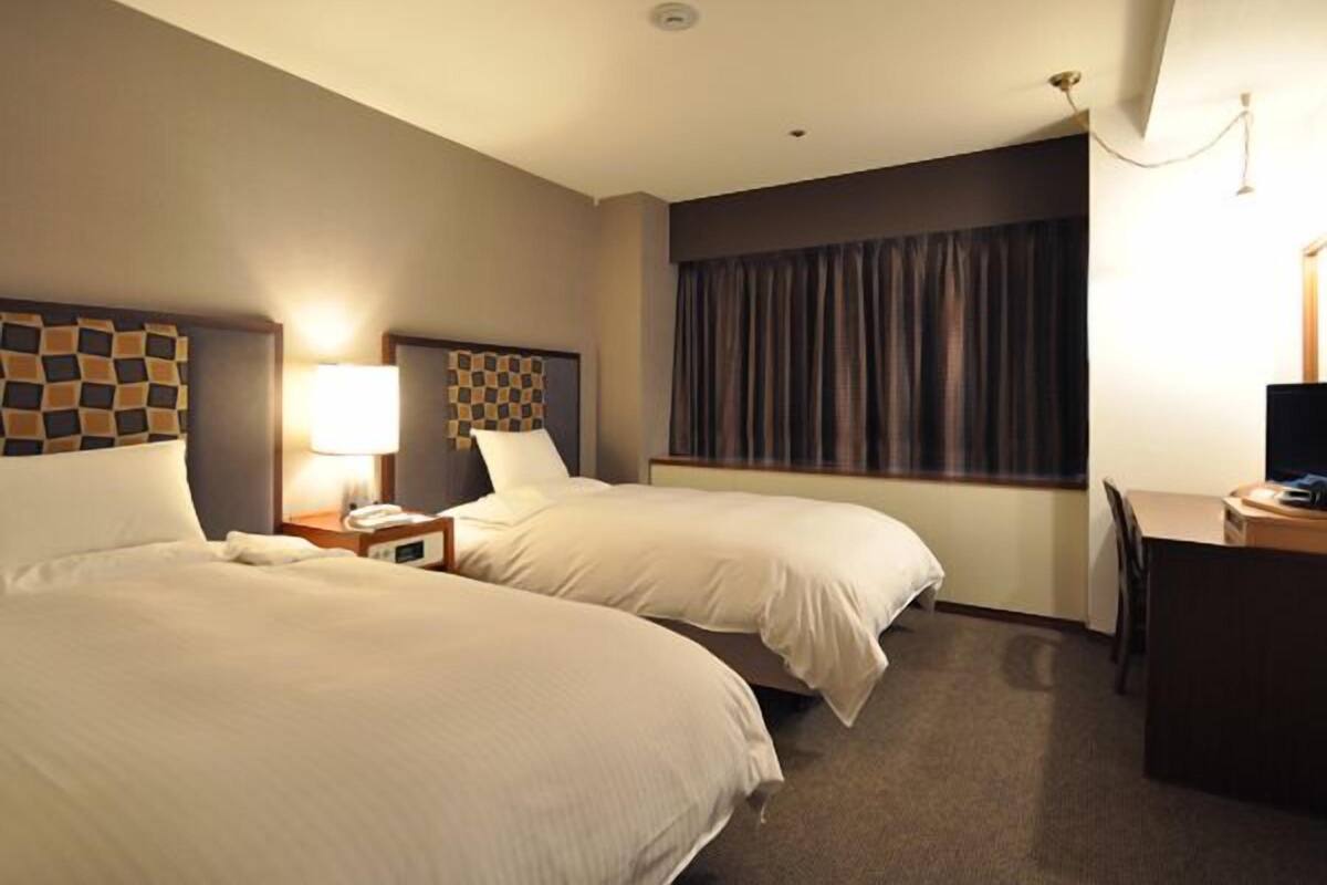 A hotel room with two beds, a desk, and a window with curtains.