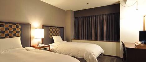 A hotel room with two beds, a desk, and a window with curtains.