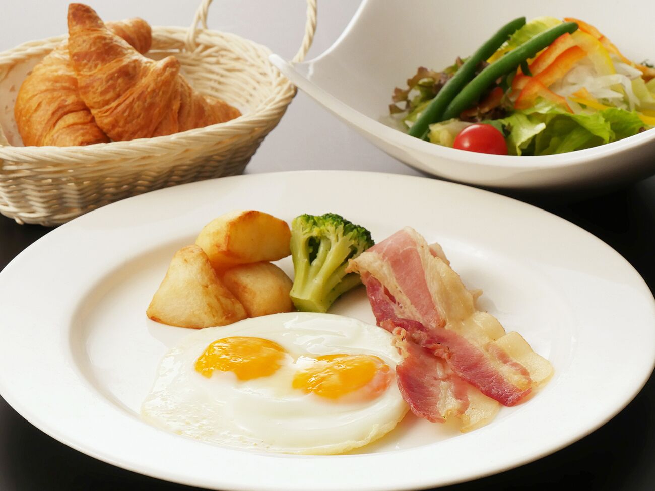 A plate with eggs, bacon, potatoes, and broccoli.