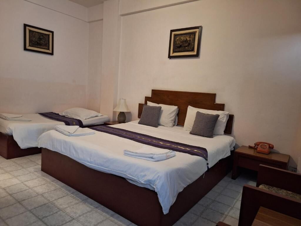 Une chambre d’hôtel avec deux lits, une tête de lit en bois, une table de chevet avec une lampe et un téléphone.