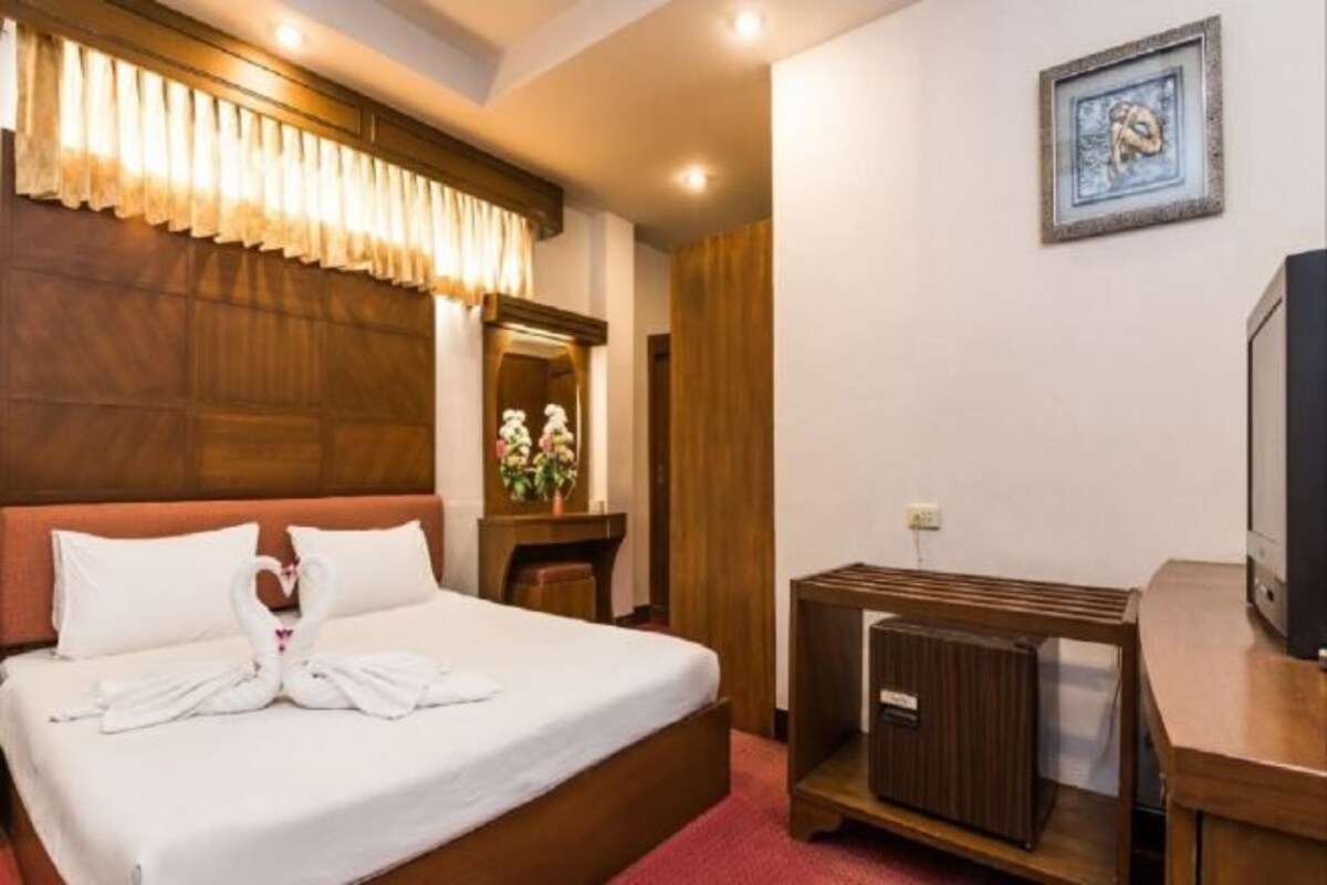 Una camera d'albergo con un letto, un comodino, una televisione e uno specchio.