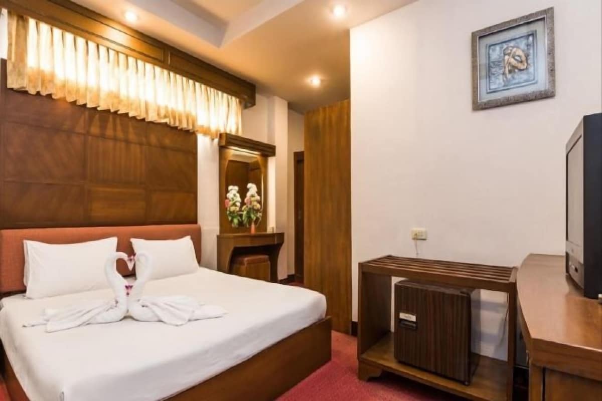 Een hotelkamer met een bed, een televisie, een houten hoofdbord, een spiegel en een ingelijst schilderij aan de muur.