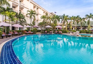 A swimming pool with lounge chairs and umbrellas, surrounded by palm trees and a building with balconies. - Romeo Palace (Pattaya)