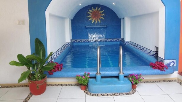 A swimming pool with a blue and white color scheme, a sun decoration, and two potted plants. - Hotel Victoria Zihuatanejo (Zihuatanejo)