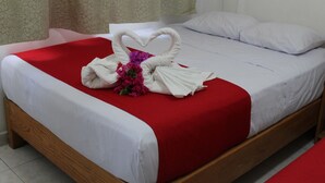 A neatly made bed with a red bedspread, white pillows, and a decorative swan made of towels with purple flowers. - Hotel Victoria Zihuatanejo (Zihuatanejo)