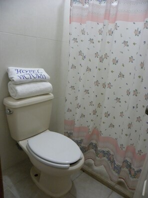A bathroom with a toilet, a rolled-up towel, and a shower curtain with a floral pattern.