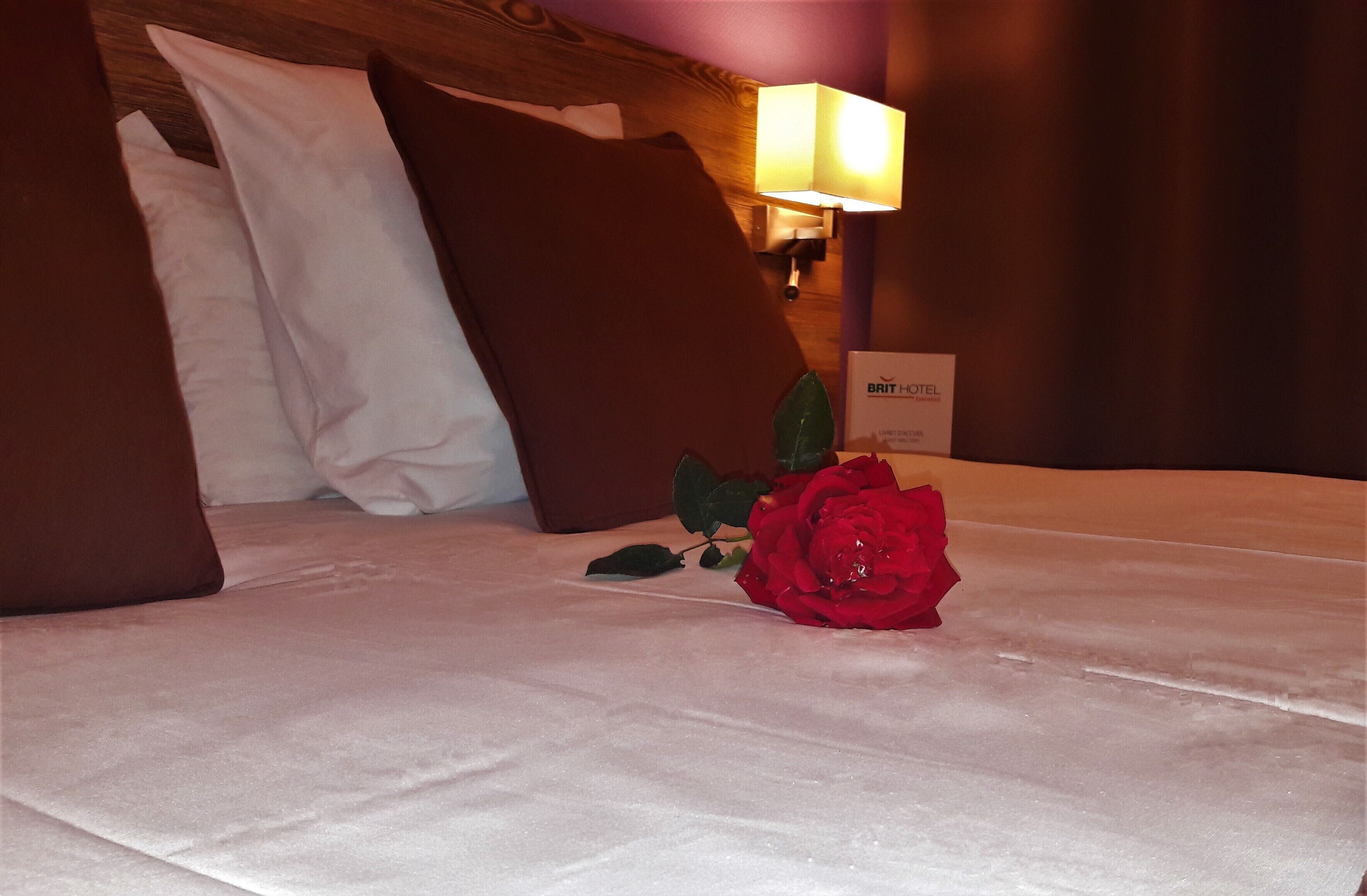 A hotel room with a neatly made bed, a bedside lamp, and a sign indicating the hotel name.