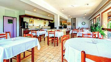 Un restaurante con varias mesas y sillas, una zona de cocina y un reloj en la pared.