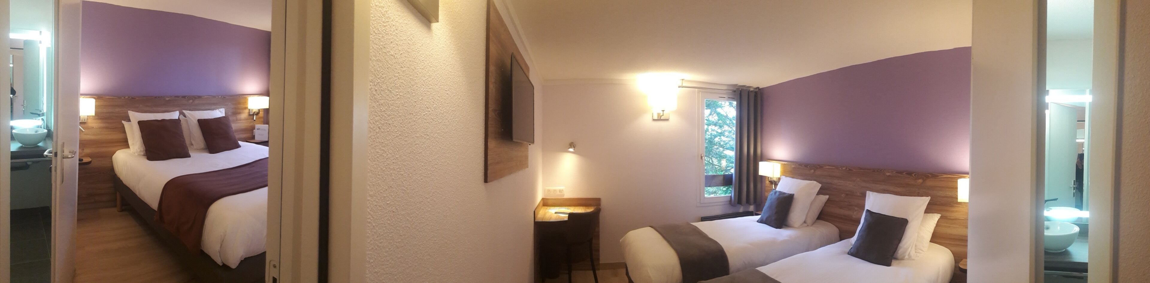 A hotel room with two beds, a window, and a bathroom visible through an open door.
