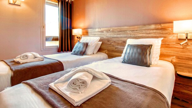 A hotel room with two beds, each with a rolled towel, a wooden headboard, and a window with curtains. - Brit Hotel Confort Pau Lons (Lons)