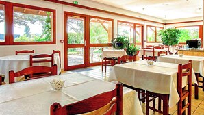 A restaurant with multiple tables and chairs, large windows, and potted plants. - Brit Hotel Confort Pau Lons (Lons)