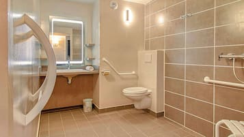 A modern bathroom with a toilet, handrails, a sink, and a mirror.