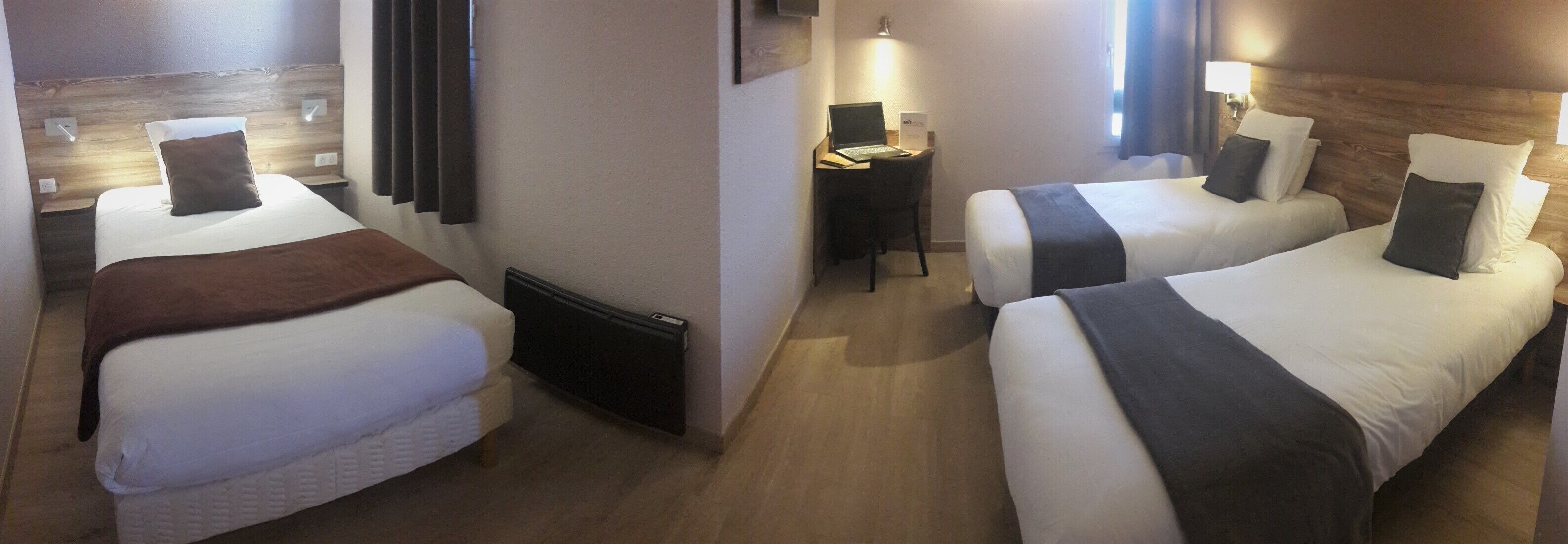 A hotel room with two single beds, a desk with a laptop, and a small seating area.