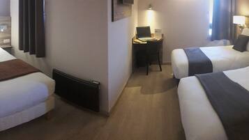 A hotel room with two single beds, a desk with a laptop, and a small seating area.