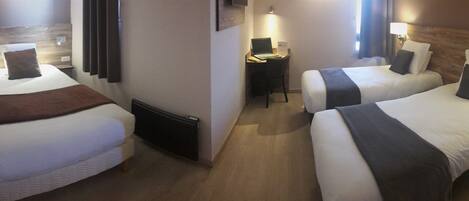 A hotel room with two single beds, a desk with a laptop, and a small seating area.